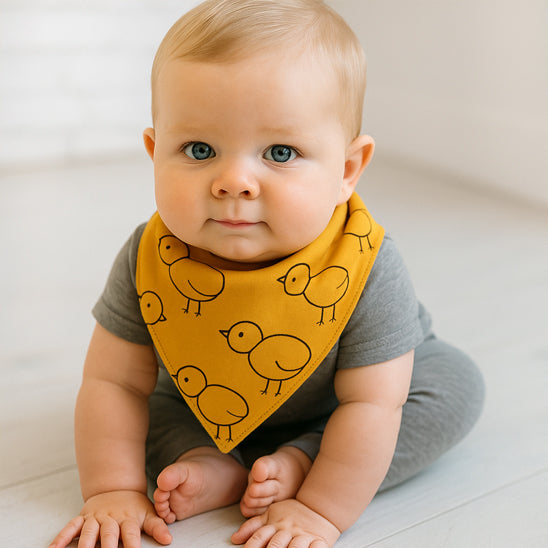 Bébé assis portant son bavoir bandana jaune aux motifs oiseaux.