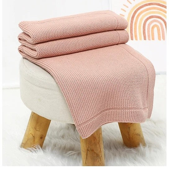 Couverture bébé en tricot rose déposée sur un tabouret.