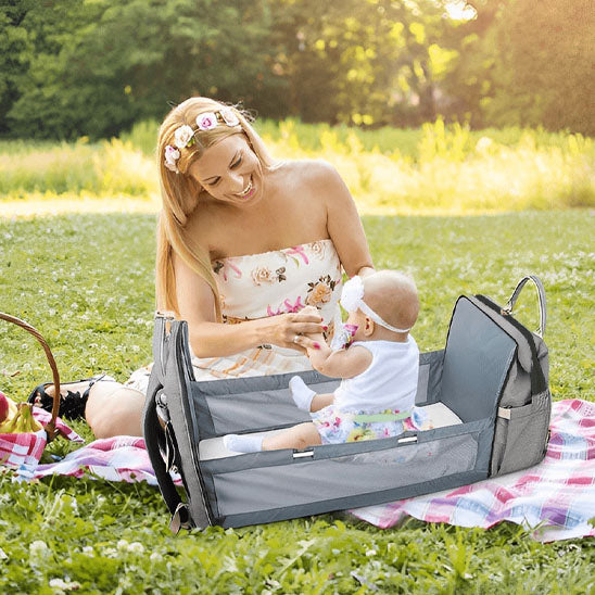 Maman assise sur herbe et bébé dans le lit du sac à dos à langer