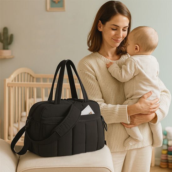 Maman dans la chambre avec bébé et son sac à langer de voyage noir.