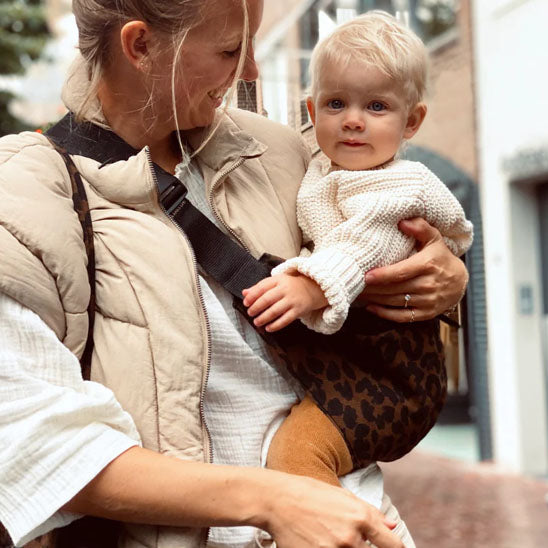 Maman heureuse de porter bébé dans porte bébé latéral léopard