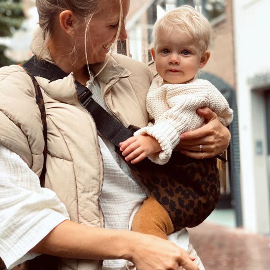 Maman heureuse de porter bébé dans son porte bébé latéral léopard.