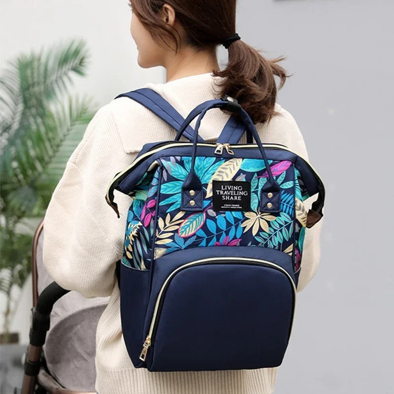 Maman portant un sac a langer bleu marine aux motifs feuilles colorées.