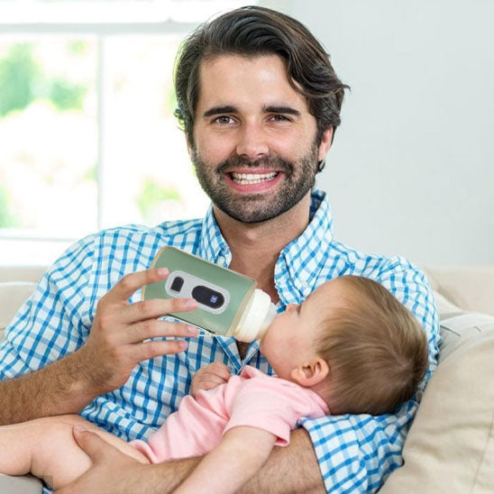 Papa donnant le biberon à bébé avec chauffe biberon portable