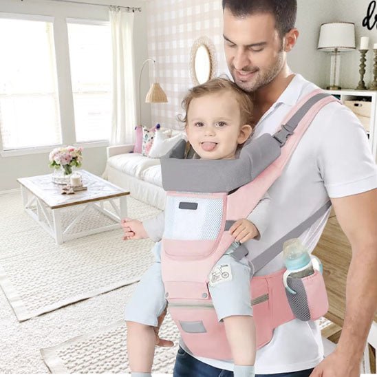 Papa portant son bambin dans un porte bébé évolutif rose.