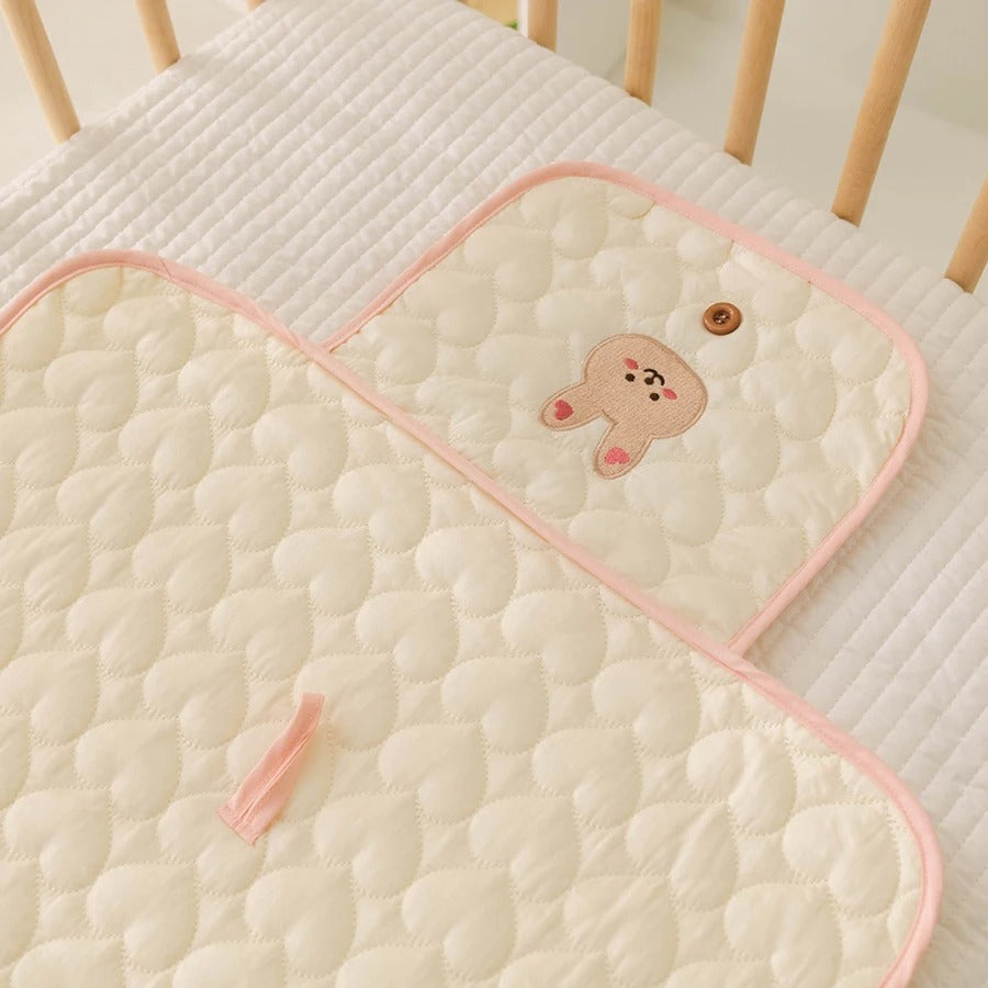 Tapis à langer nomade vanille avec bordures roses et lapin.