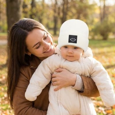 Bébé dans les bras de maman portant son bonnet bebe blanc.