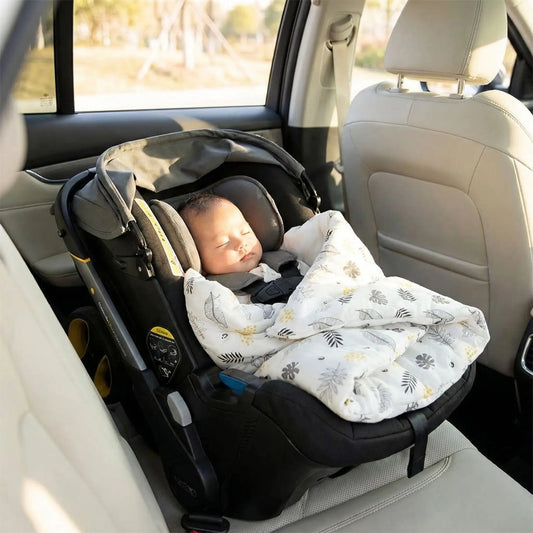 Bébé endormi dans son nid d'ange siege auto aux motifs feuilles.