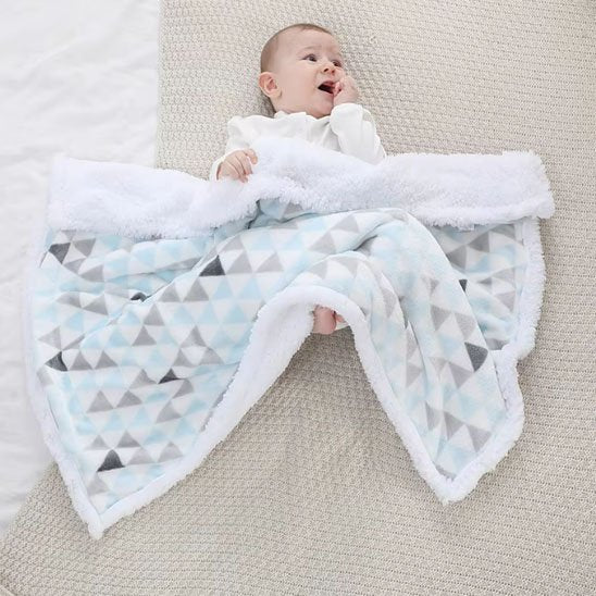 Bébé étendu au sol avec sa couverture polaire bleue aux motifs triangles.