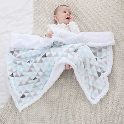 Bébé étendu au sol avec sa couverture polaire bleue aux motifs triangles.