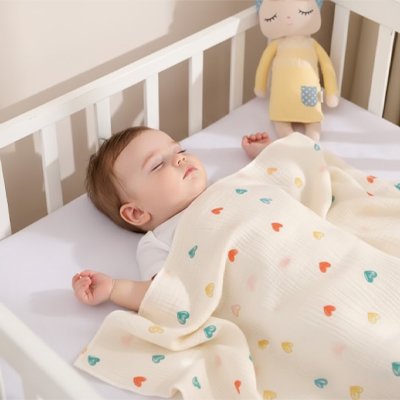 Bébé qui dort confortablement avec sa couverture bébé aux motifs coeurs.