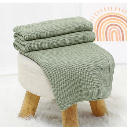 Couverture bébé de couleur sauge déposée sur un tabouret.