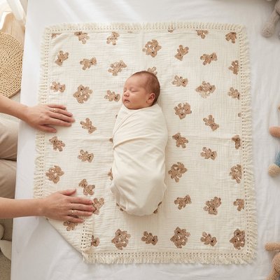 Couverture bébé en mousseline ornée de pompoms.