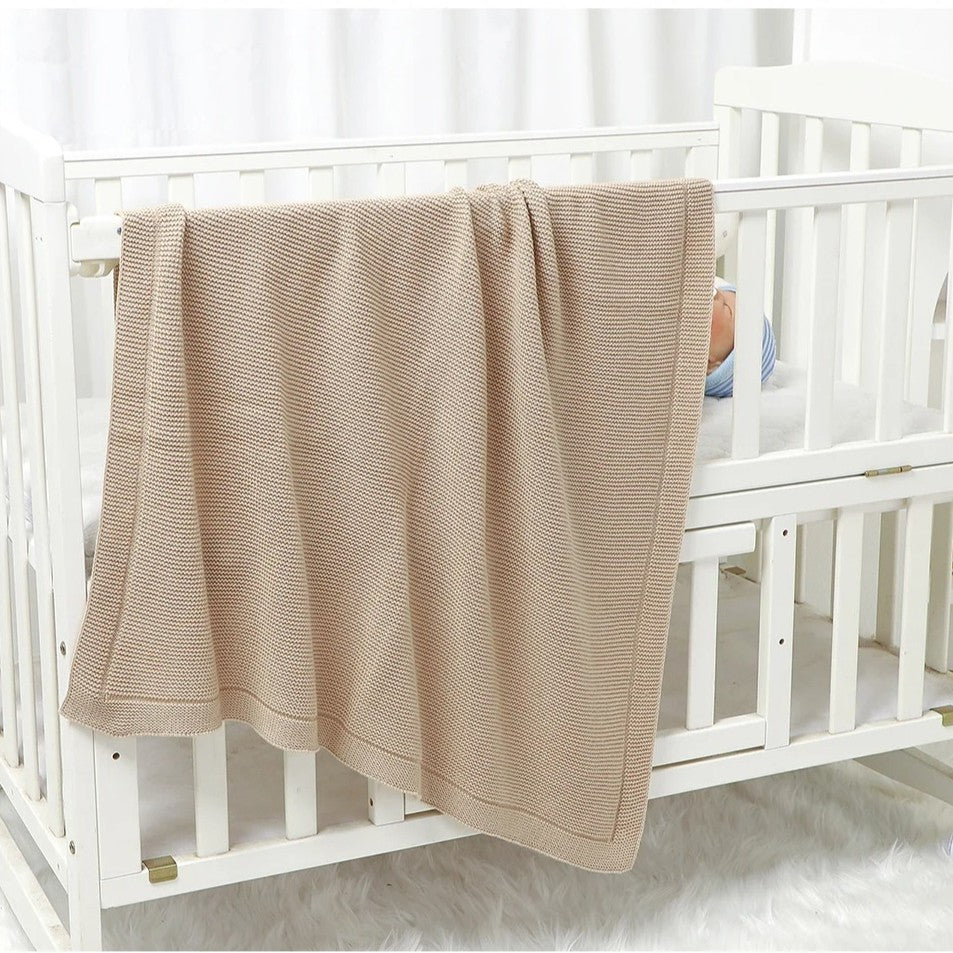 Couverture bébé tricot beige déposée sur lit bébé