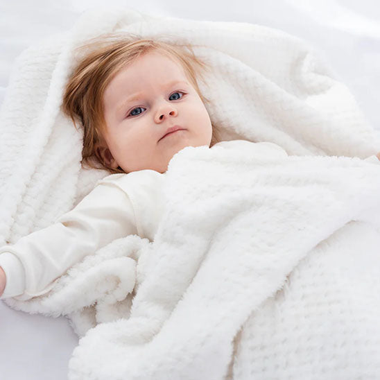 Enfant confortable couché sous sa couverture bebe blanche.