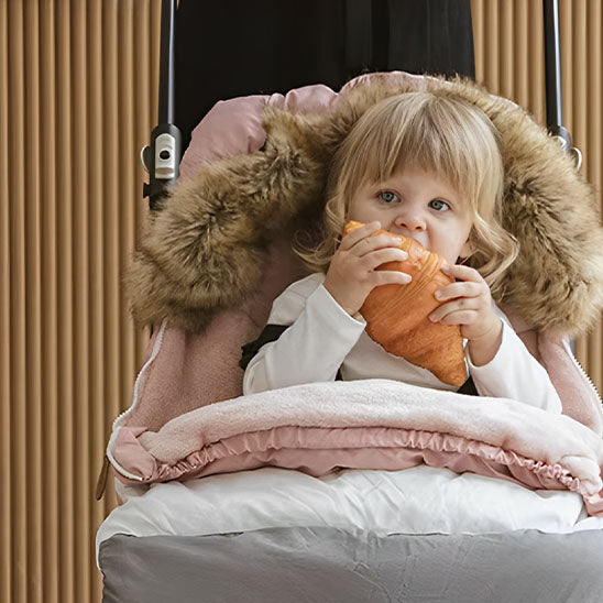 Enfant mangeant son croissant dans sa chancelière Nordica.