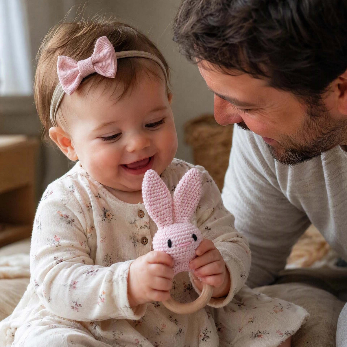 Hochet bébé lapin en tricot rose avec poignée en bois naturel.