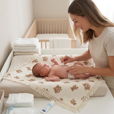 Maman change son bébé sur sa couverture bébé en mousseline.