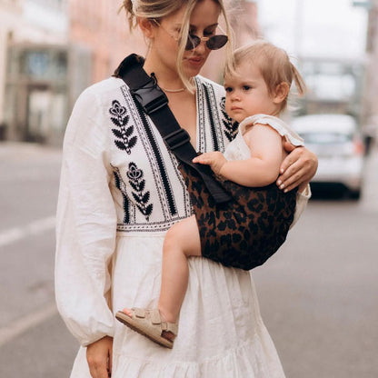 Maman en ville portant bébé avec porte bébé latéral léopard
