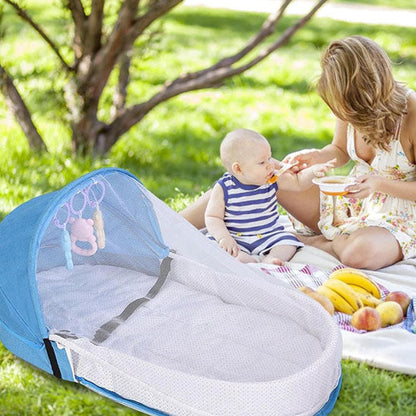Maman et bébé en pique-nique avec un lit bebe de voyage bleu.