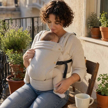 Maman relaxant à l'extérieur portant un porte bebe beige écru.