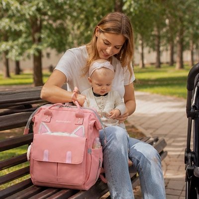 Maman sur un banc de parc avec son sac a dos a langer chat rose.