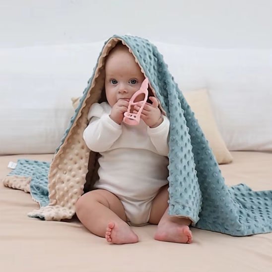 Mignon petit bébé rigolo avec sa couverture bebe sur la tête.
