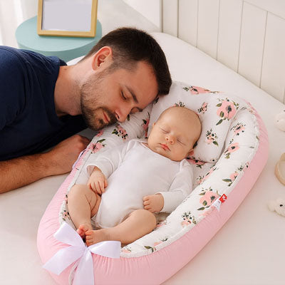 Papa endormi et bébé dans son nid d ange rose à motifs fleuris.